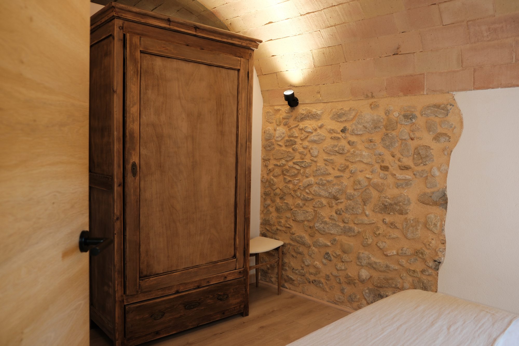 Habitació 1 — armari antic i mur de pedra vista